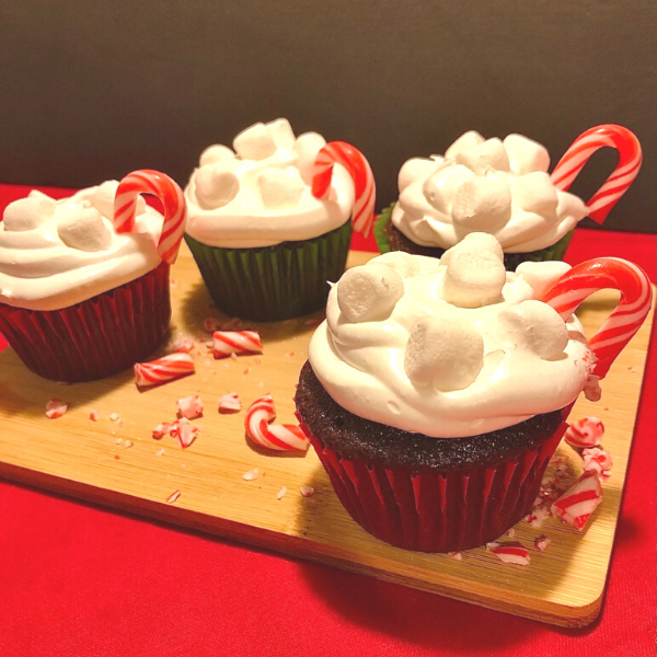 4 cupcakes with red and green  wrappers, icing with mini marshmallows and a candy cane in them.