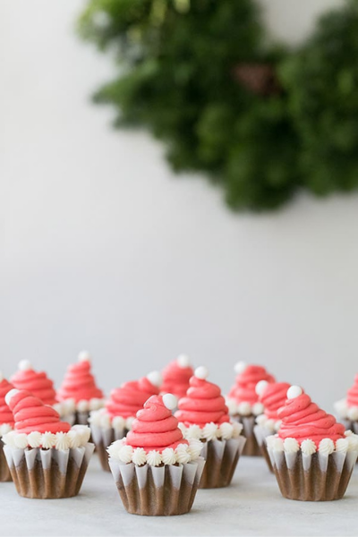 10 Gingerbread flavored cupcakes with red and white icing to look like a Santa hat with a green wreath in the background