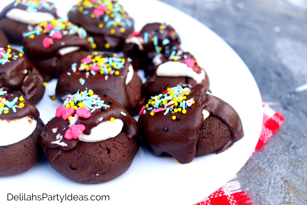 White plate of hot cocoa cookies, with colored sprinkles on top of brown icing