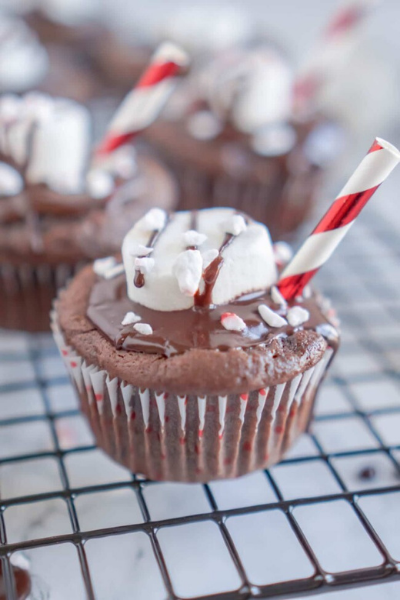 Hot chocolate cupcake on a wire rack with marshmallow on top with red and white straw sticking out.