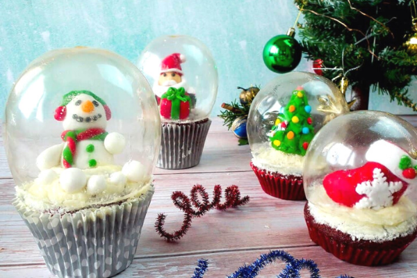4 cupcakes all with gelatin slow globes over different Christmas Ornaments made from icing - snowman, Stocking, Christmas Tree, Santa and a gift