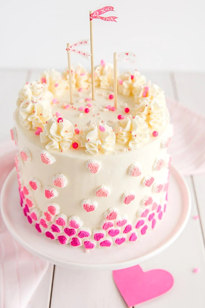 Beautiful white cake with pink hearts and pink and red sprinkles on a white cake stand