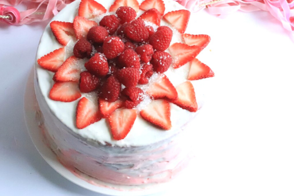 Beautiful Strawberry Poke Cake decorated in white icing with strawberries and raspberries on the top