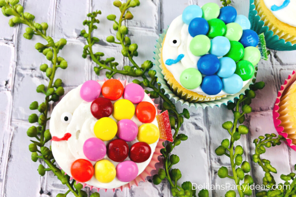 2 Cute Fish Cupcakes one with red, pink orange and yellow M & M's as scales and the other with blue and Green M & M's