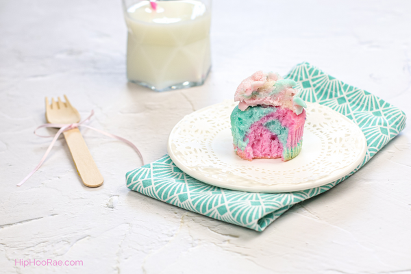 Cotton candy cupcake cut in half on white plate with cup of milk