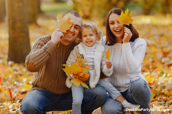 Family of 3 holding maple leaves while posing for a photo