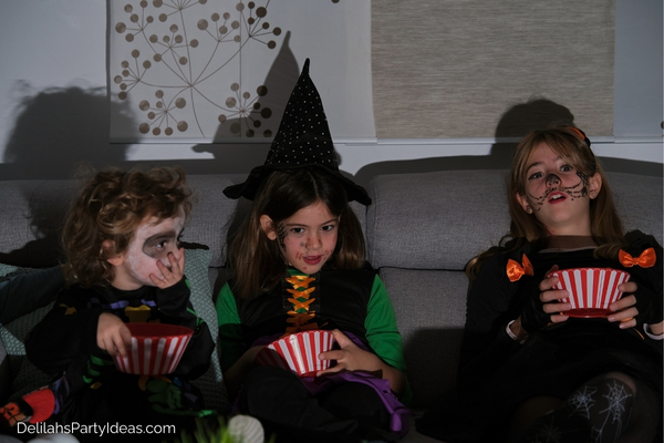 3 kids eating popcorn during halloween family movie night