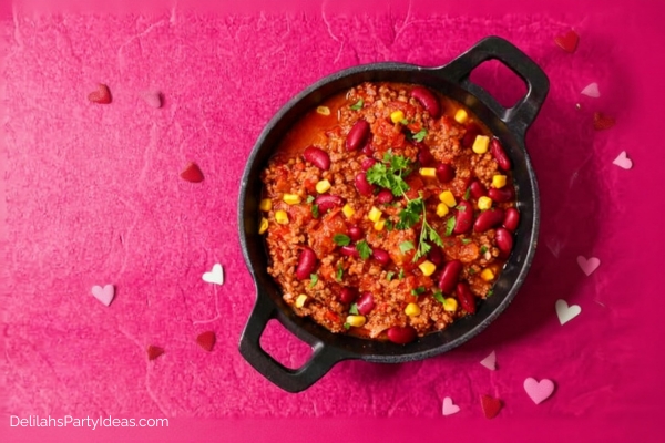 bowl of chili con carne on pink table littered with cut out paper hearts q